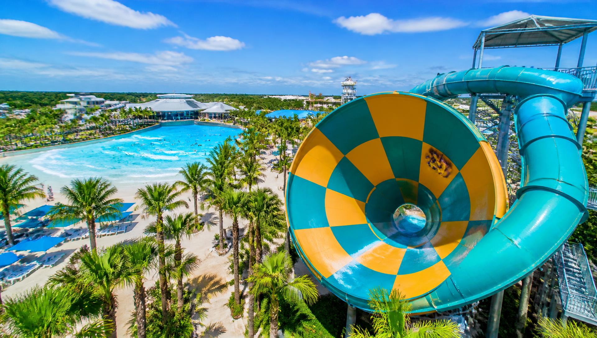Aerial view of a teal and yellow funnel water slide beside a turquoise wave pool